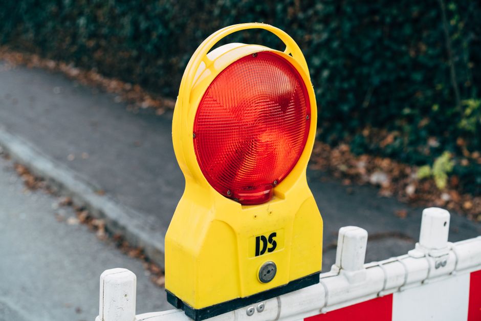 A construction roadblock featuring a white plastic safety barrier with red reflective stripes and yellow warning lights on top of two vertical posts surrounds a section of roadway outside a residentia